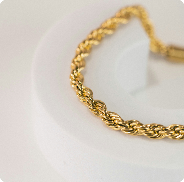 Bracelet en or tressé posé sur un fond blanc.